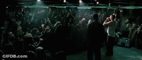 Two Men Are Standing On Stage In Front Of A Crowd Of People GIF