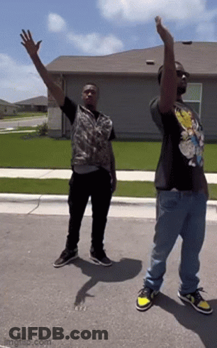Two Men Are Standing On The Side Of The Road With Their Arms Up In The Air . GIF