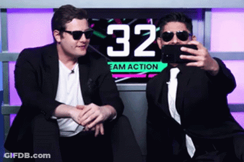 Two Men Are Taking A Selfie In Front Of A Sign That Says 32 GIF