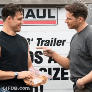 Two Men Are Talking In Front Of A Trailer Size Sign GIF