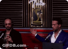 Two Men Are Talking To Each Other In Front Of A Sign That Says Tate GIF