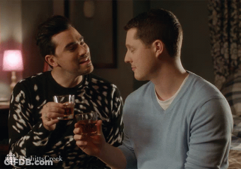 Two Men Are Toasting With Glasses Of Whiskey And The Word Schitts Creek Is On The Bottom Right GIF