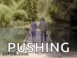 Two Men Are Walking Across A Bridge With The Word Pushing In The Background . GIF