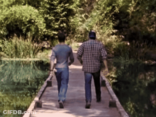 Two Men Are Walking Across A Wooden Bridge GIF