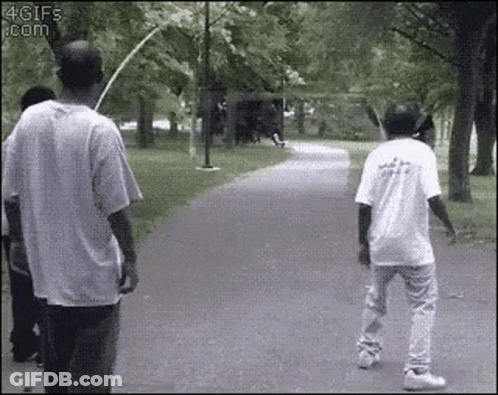 Two Men Are Walking Down A Path In A Park . One Of The Men Is Holding A Bat . GIF