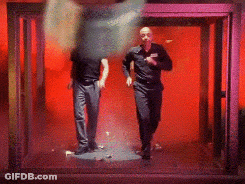Two Men Are Walking Through A Doorway In A Dark Room GIF