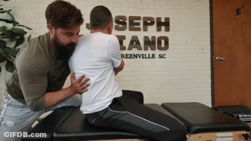 Two Men Are Working On A Man 'S Back In Front Of A Sign That Says Joseph Tano Reenville Sc GIF