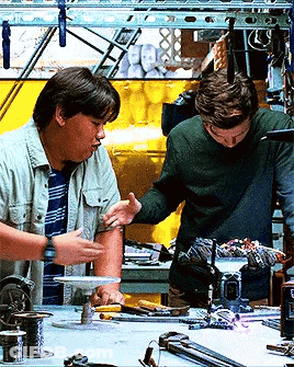 Two Men Are Working On A Project In A Workshop And One Of Them Is Touching Another Man 'S Arm GIF