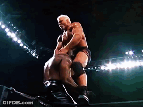Two Men Are Wrestling In A Dark Stadium With Lights Behind Them . GIF