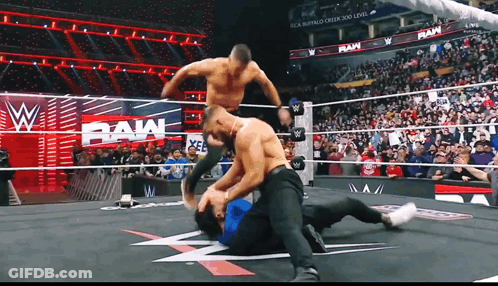 Two Men Are Wrestling In A Wrestling Ring With A Crowd Watching And A Sign That Says Raw GIF