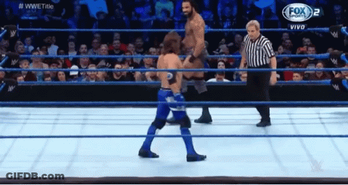 Two Men Are Wrestling In A Wrestling Ring With A Referee In The Background . GIF