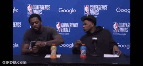 Two Men At Table In Front Of Conference Finals Sign GIF