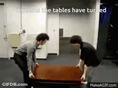 Two Men Carrying A Table That Says It Seems The Tables Have Turned On Makeagif.com GIF