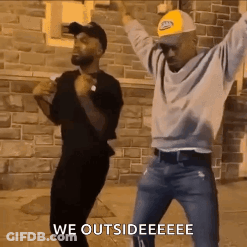 Two Men Dancing Arms Raised Brick Building GIF