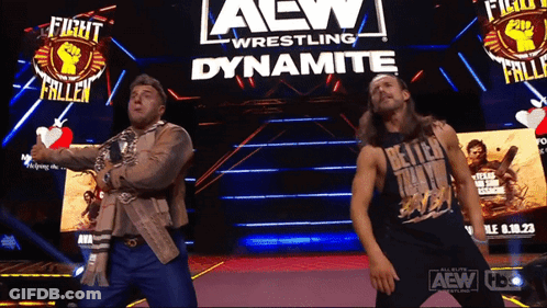 Two Men Dancing In Front Of Dynamite Wrestling Sign GIF