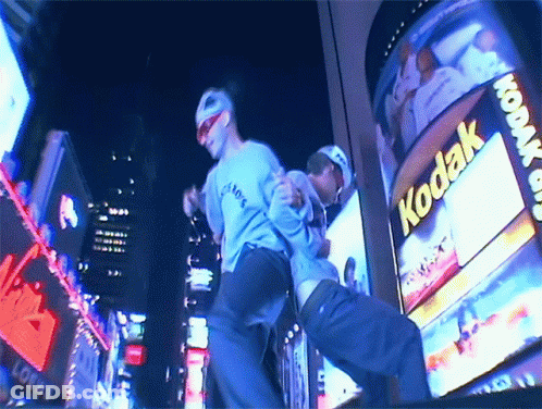 Two Men Dancing In Front Of Kodak Billboard GIF