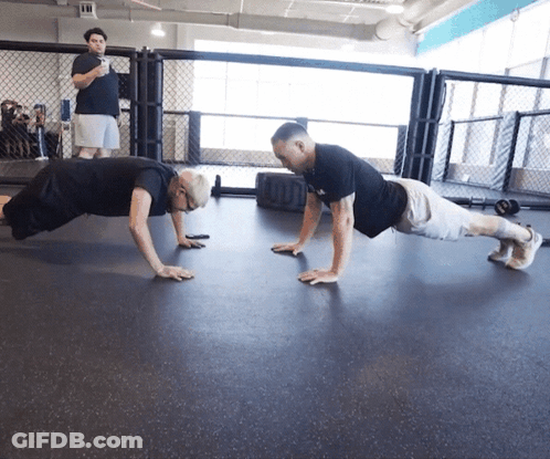 Two Men Do Push Ups In A Gym With A Man Standing Behind Them GIF