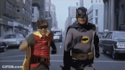 Two Men Dressed As Batman And Robin Walking Down Street GIF