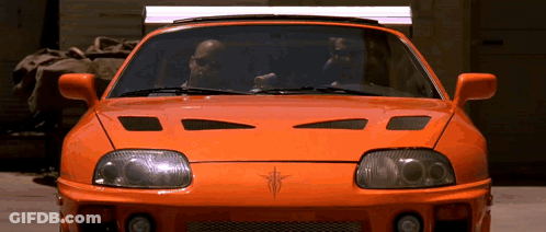 Two Men Driving Orange Sports Car In Garage GIF