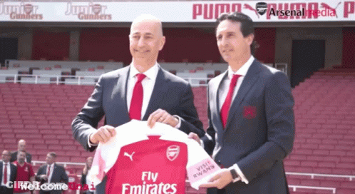 Two Men Holding Fly Emirates Jersey In Front Of Puma Banner GIF