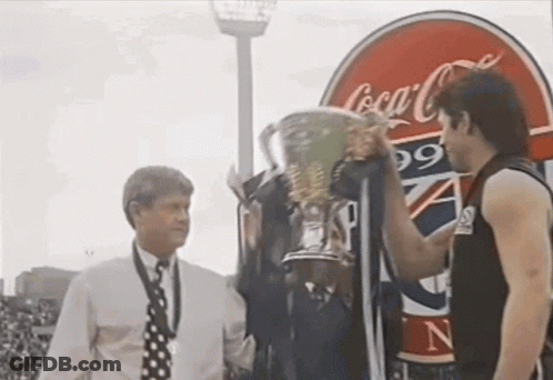 Two Men Holding Trophy In Front Of Coca-Cola Sign GIF