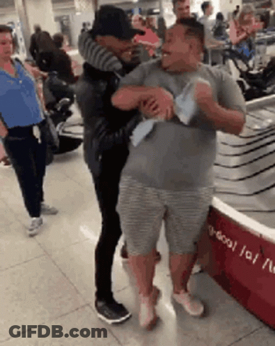 Two Men Hugging At Airport Woman Watches GIF