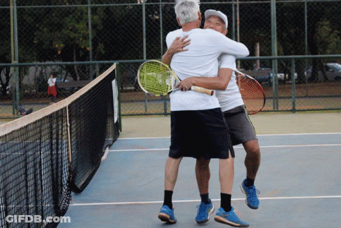 Two Men Hugging Each Other On A Tennis Court With Rackets In Their Hands GIF