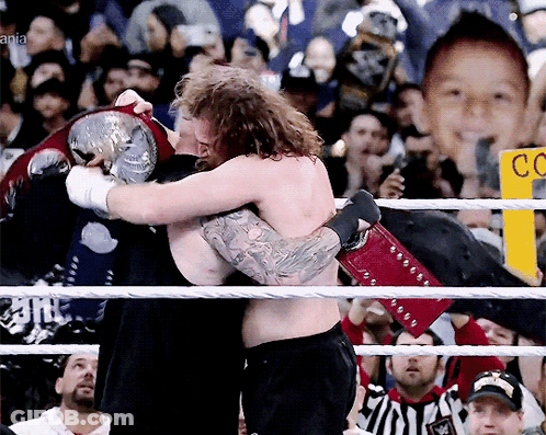 Two Men Hugging In A Wrestling Ring With A Sign That Says Cc On It GIF