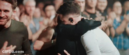Two Men Hugging In Front Of A Crowd Of People GIF