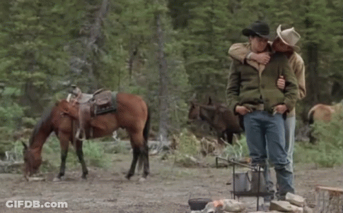 Two Men Hugging In Front Of A Horse In A Field GIF