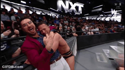 Two Men Hugging In Front Of NXT Sign GIF