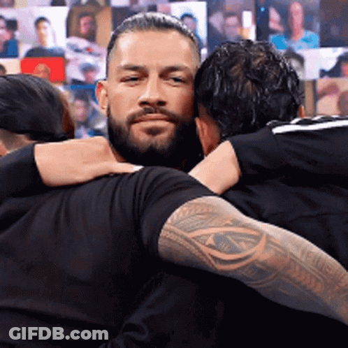 Two Men Hugging In Front Of Wall Of Pictures GIF