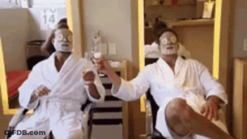 Two Men In Bathrobes With Face Masks On Their Faces Are Sitting In A Chair . GIF