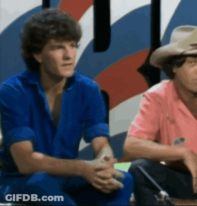 Two Men In Blue And Pink Shirts Sitting GIF