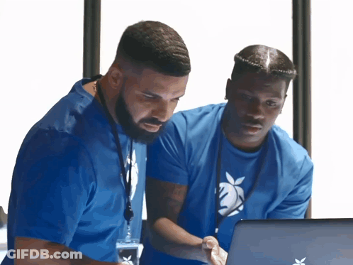 Two Men In Blue Shirts Are Looking At A Laptop Computer GIF