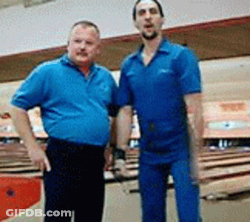 Two Men In Blue Shirts Are Posing For A Picture In A Bowling Alley GIF