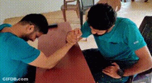 Two Men In Blue Shirts Arm Wrestling GIF