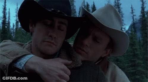 Two Men In Cowboy Hats Hugging Each Other In A Forest GIF
