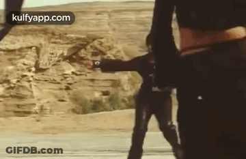Two Men In Desert One Holding Gun GIF