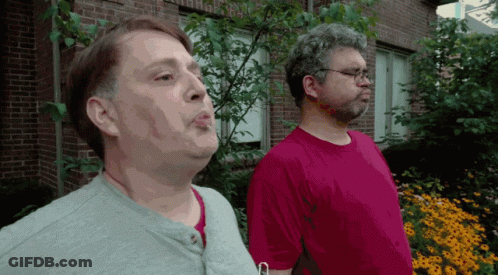 Two Men In Front Of Brick Building With Flowers GIF