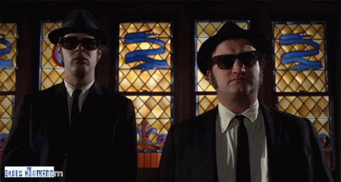 Two Men In Front Of Stained Glass Window With Words The Blues Brothers GIF