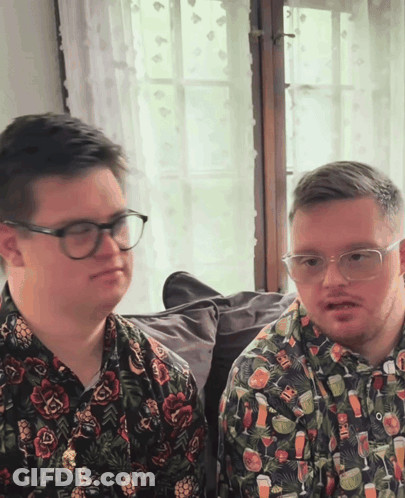 Two Men In Glasses And Drink Shirts Sitting Together GIF