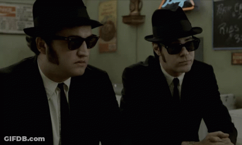 Two Men In Hats And Sunglasses Beside Coca Cola Chalkboard GIF