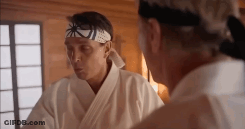 Two Men In Karate Uniforms Are Standing Next To Each Other In A Room And Talking . GIF