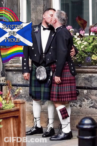 Two Men In Kilts Kiss In Front Of A Sign That Says " Scottish And Proud " GIF