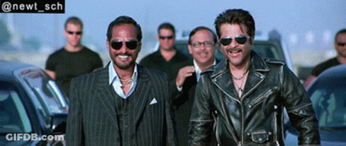 Two Men In Leather Jackets And Sunglasses Smiling Near Cars GIF