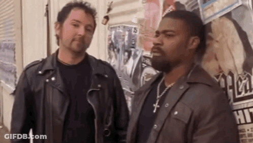 Two Men In Leather Jackets Are Standing Next To Each Other In Front Of A Wall Covered In Posters . GIF