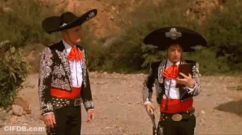 Two Men In Mariachi Outfits Are Standing Next To Each Other On A Dirt Road GIF