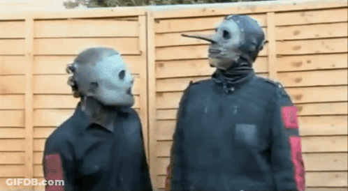 Two Men In Masks Standing In Front Of Wooden Fence GIF