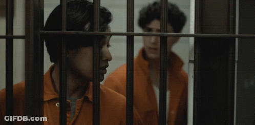 Two Men In Orange Jumpsuits Behind Bars GIF